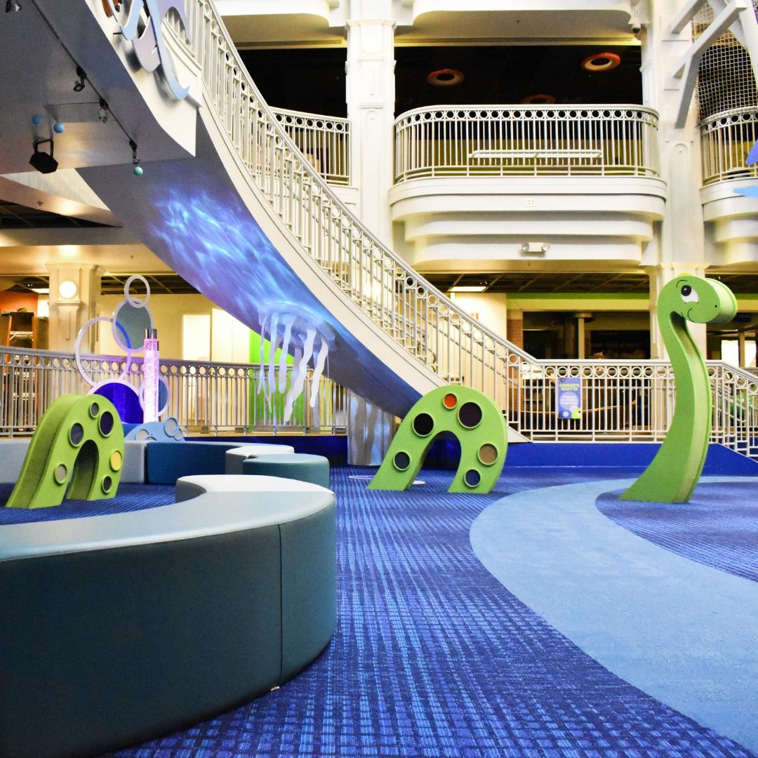 Safe flooring for museums with custom printed carpet and green water dinosaur play equipment.