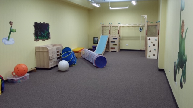 Safe flooring for kids at a community center playroom. There is a small wooden playground, and several tunnels for children to play in.