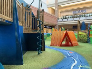 Custom designed carpeting with a river scene at an indoor mall play area. This play area has a few play structures and an orange tent.
