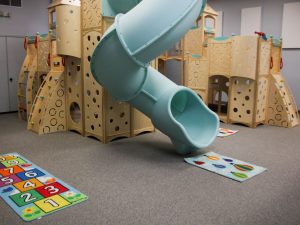 Indoor playground with a blue slide and long lasting impact absorbing carpeting.