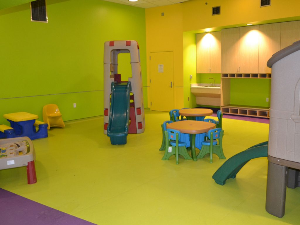 Bright green and purple SafeLandings Resilient Sheet Vinyl System at an indoor day care with small tables and several plastic play equipment.